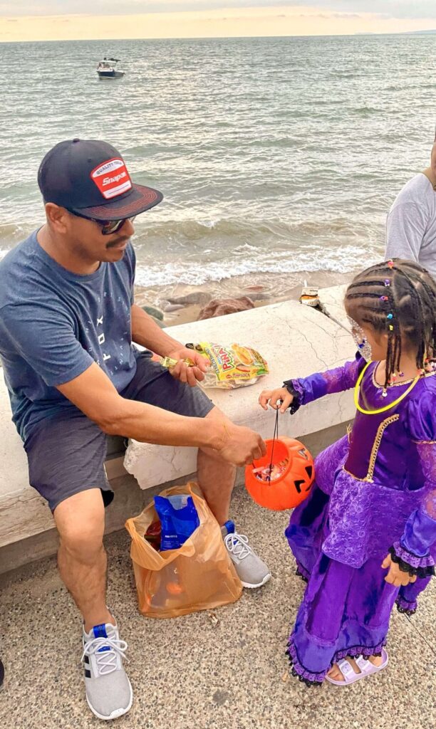 Mario giving candy to a child in a costume on the boardwalk in Puerto Vallarta during the Dia de los Muertos celebrations.